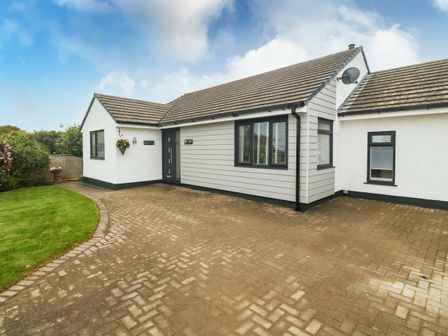 A detached single story house with a paved driveway and a small lawn in front at Bwthyn Eirlys Snowdrop Cottage in Cemaes Bay