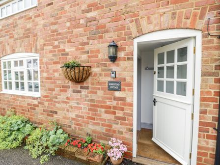 The entrance door to a brick building with a window planter and flowers by the door at Homestead Cottage in Halford