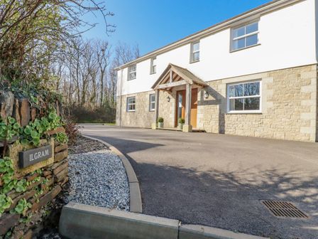 The exterior of a two story house with stone and white walls a curved driveway and a wooden porch at Ilgram in St Newlyn East