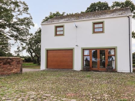 A white two-story building with a brown garage door and double glass doors with potted plants on a cobblestone driveway at Bramblewood Cottage in Crookdake near Bassenthwaite