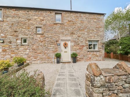 A stone cottage with a pathway leading to a door decorated with a wreath at Bella Cottage Bolton near Appleby-in-Westmorland