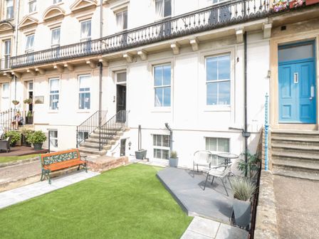An outdoor area with stairs leading to building entrances a bench artificial grass and a small patio with two chairs and a table at Sunset View in Whitby