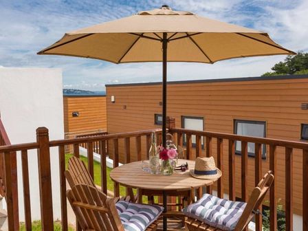 A balcony with a round wooden table and two chairs under a large umbrella at Egret in Brixham