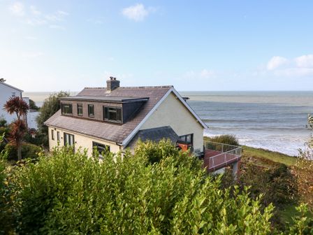 A house with a balcony overlooking the sea surrounded by greenery at Machlud Haul in Llwyngwril
