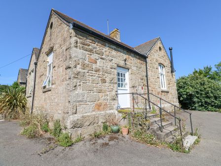 Stone building with steps and a white door surrounded by plants and a paved area at The Cottage in Ludgvan near Crowlas