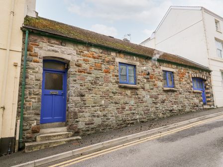 A stone building with blue doors and windows along a sloped street at Llys-Yr-Onnen in Carmarthen
