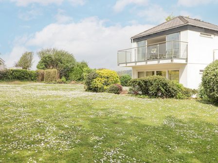 A white two-story house with glass balcony and a large garden with bushes and small white flowers at 17 Coedrath Park in Saundersfoot