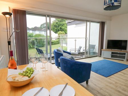 A living room with blue chairs a wooden table with bread grapes and wine and a television at 28 Coedrath Park in Saundersfoot