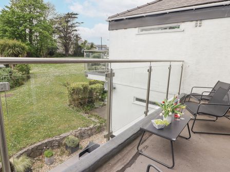 A balcony with two black chairs and a small table holding flowers grapes and drinks overlooking a garden at 26 Coedrath Park Saundersfoot