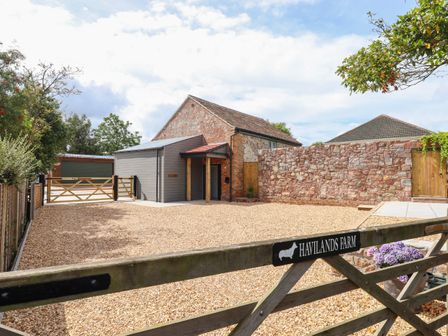 A farm entrance with a wooden gate and gravel driveway leading to a brick and wood building at Havilands Farm