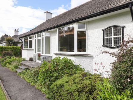 Exterior view of a white house with large windows surrounded by bushes and plants at Halewood in Bowness-On-Windermere