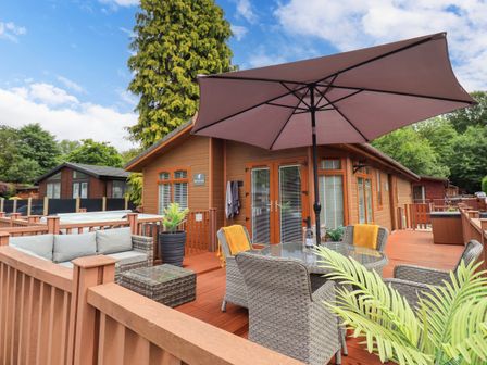 An outdoor wooden deck with wicker furniture and a large umbrella at Black Dog Lodge Thirlmere 3 White Cross Bay near Windermere