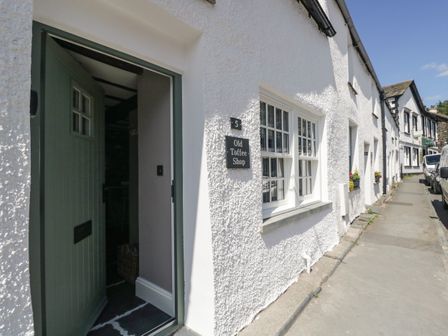 A street view of a white building with an open green door and windows with flower boxes at Old Toffee Shop in Ambleside