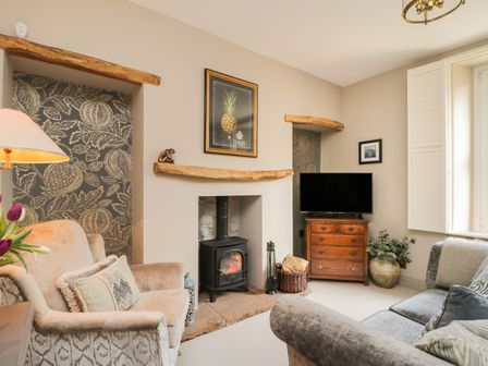 A living room with a wood stove fireplace a television on a wooden chest and seating at Hideaway Cottage in Penrith