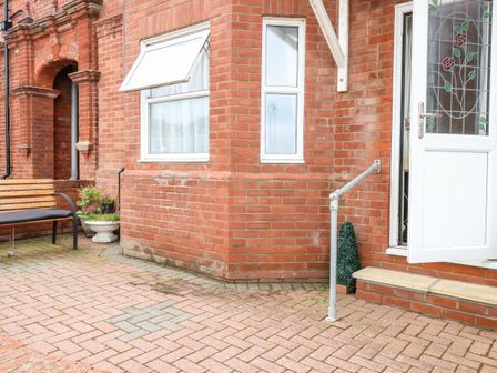 A brick patio with a bench flower pots and a white door with stained glass at Ellan Vannin in Sheringham