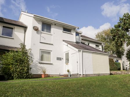 A white two-story house with windows and a door on a grassy area at Llewoc Cuddfan in Y Felinheli
