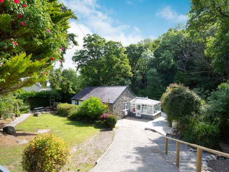 A stone cottage with a glass conservatory surrounded by trees and garden at Nant Cottage in Rowen