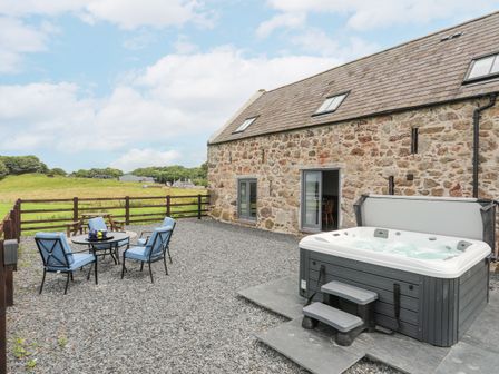 An outdoor patio with a hot tub and a seating area with four blue cushioned chairs at Gwel Y Fenai in Y Felinheli