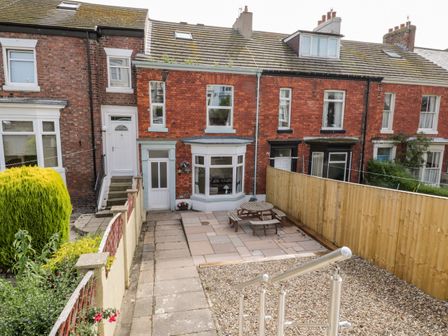 A backyard with a patio table and benches paved area and gravel section behind a row of brick houses at Harbour Hideaway in Whitby