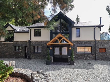 A stone and stucco house with large windows and a wooden porch at Hares Breath in Bowness On Windermere