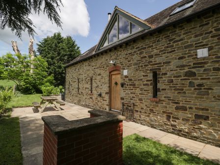 The exterior of a stone house with a wooden door a paved patio area with a picnic table and surrounding greenery at The Coach House in Ludlow