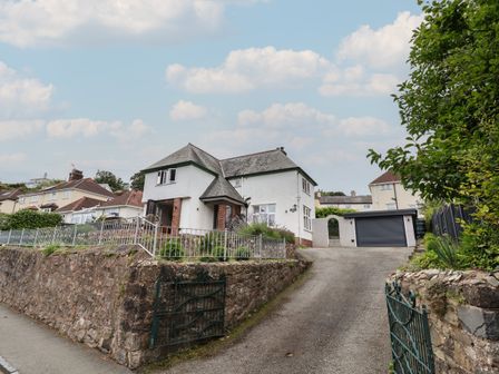 A white house with a sloped roof and a driveway leading to a garage at Bryn Gwynedd in Conwy