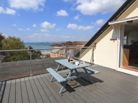 A balcony with a picnic table and drinks overlooking the sea at Shippen in Hope Cove