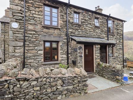 Stone house with wooden door and windows and a low stone wall at The Curious Orange in Troutbeck