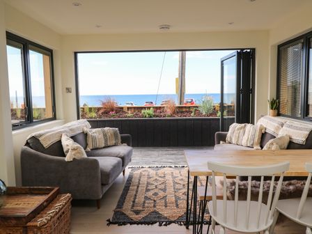 A sitting area with two sofas and a dining table with chairs overlooking the sea at Sandpiper Chalet in Eype