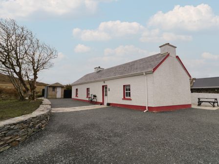 A white cottage with red trim and a bike outside near a stone wall at Teach Phaidi Mhoir in Glencolumbkille County Donegal