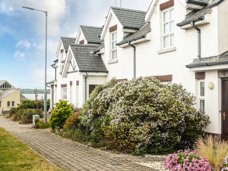 A row of white houses with slate roofs and bushes along a sidewalk at Beach View in Duncannon near Ramsgrange County Wexford