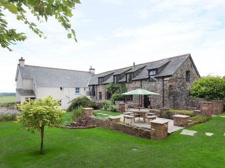 A house with stone and white walls and a garden with a picnic table and green umbrella at Honey Bee Cottage in Bradworthy