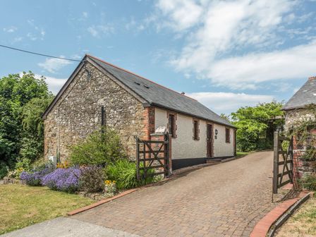 A stone and brick cottage with a driveway and garden with flowers at Woodpecker Cottage in Bradworthy near Bude