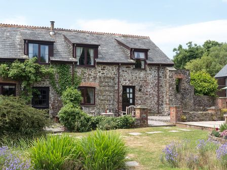 A stone cottage with ivy on the walls and a garden with grass and flowers at Greenfinch in Bradworthy near Bude