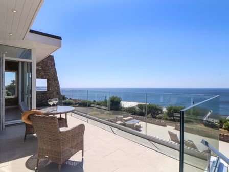 A balcony with two wicker chairs and a table with two glasses overlooking the sea at Boscregan in Porthleven