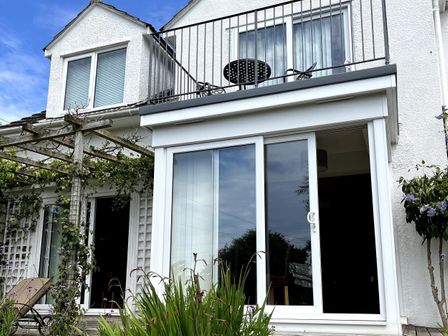 Exterior view of a white two-story house with balcony and sliding glass doors with plants in front at Linden Lea in Newton Ferrers