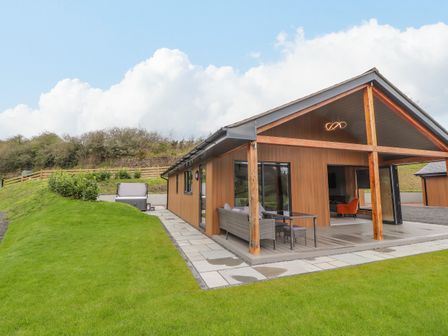 An exterior view of a wooden house with a covered patio and outdoor seating on a lawn at Pool View in Meifod Powys