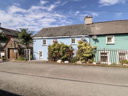 A row of houses with blue and green walls and small windows with bushes and a metal fence in front at 1 The Terrace Rosebush near Newport Pembrokeshire