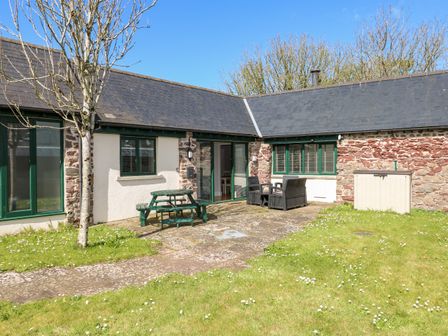 An outdoor patio with green picnic table and chairs next to a stone house with green window frames at Ramsey Cottage in Milford Haven