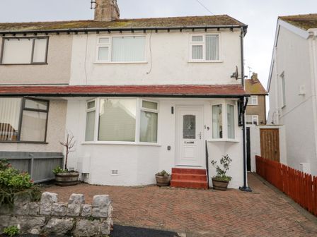 A semi detached house with a white front door and bay windows with a brick driveway at The Crescent Escape in Rhos On Sea
