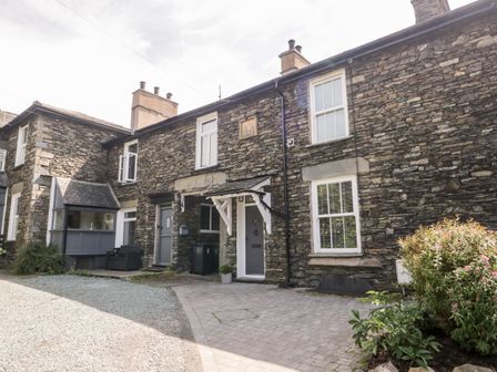 A stone exterior of a house with windows a door a small porch and bushes at The Burrow in Windermere