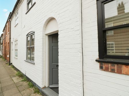 A white brick exterior of a house with a partially open grey door and windows with black frames at 5 Bull Street in Stratford-Upon-Avon