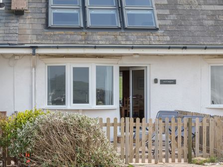 The front of a house with three upstairs windows a white door with glass panels a wooden fence and two lounge chairs at Sea Campion in Thurlestone