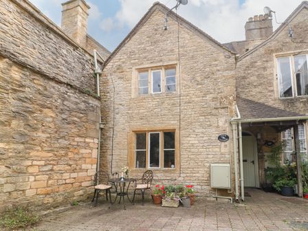 A stone cottage exterior with a small table and two chairs and potted plants at Coln Cottage in Stow-On-The-Wold