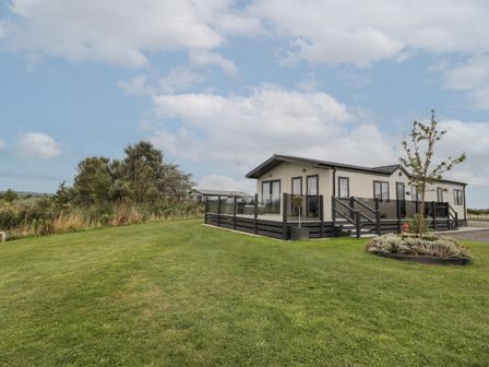 A modular or manufactured home with a fenced deck on a manicured lawn with trees and shrubs at 14 Fairways in Burnham-On-Sea