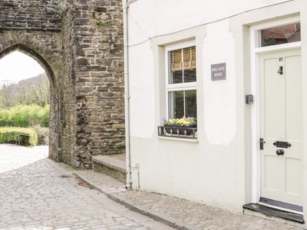 Exterior of a white house with a green door and window with flowers next to a stone archway at Millgate House in Conwy