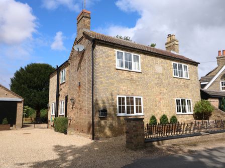A brick two-story house with white-framed windows and a gravel driveway at Coronation Cottage in Upwell