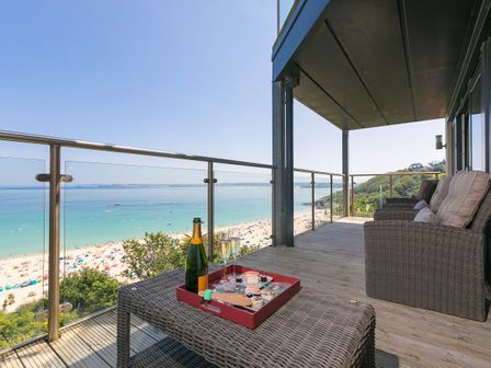 A balcony with wicker chairs a table with champagne and sushi overlooking the beach at Crystal Bay in St Ives