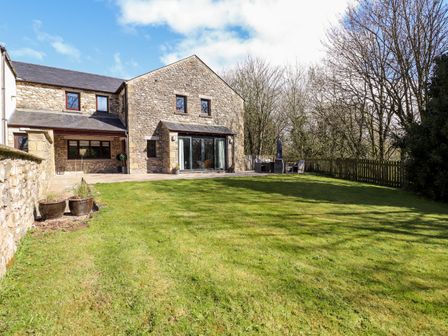 A stone house with a lawn and patio furniture in the backyard at Crooklands Cottage in Crooklands