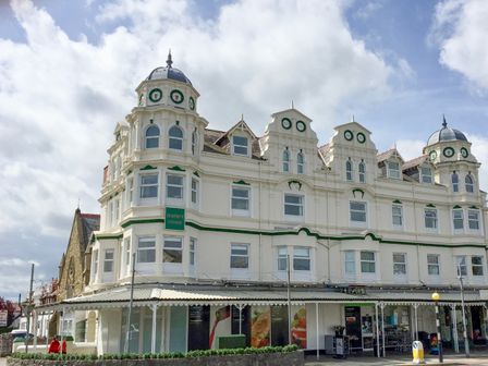 A large white building with green accents and multiple windows under a cloudy sky at Royal Manor Park in Llandudno